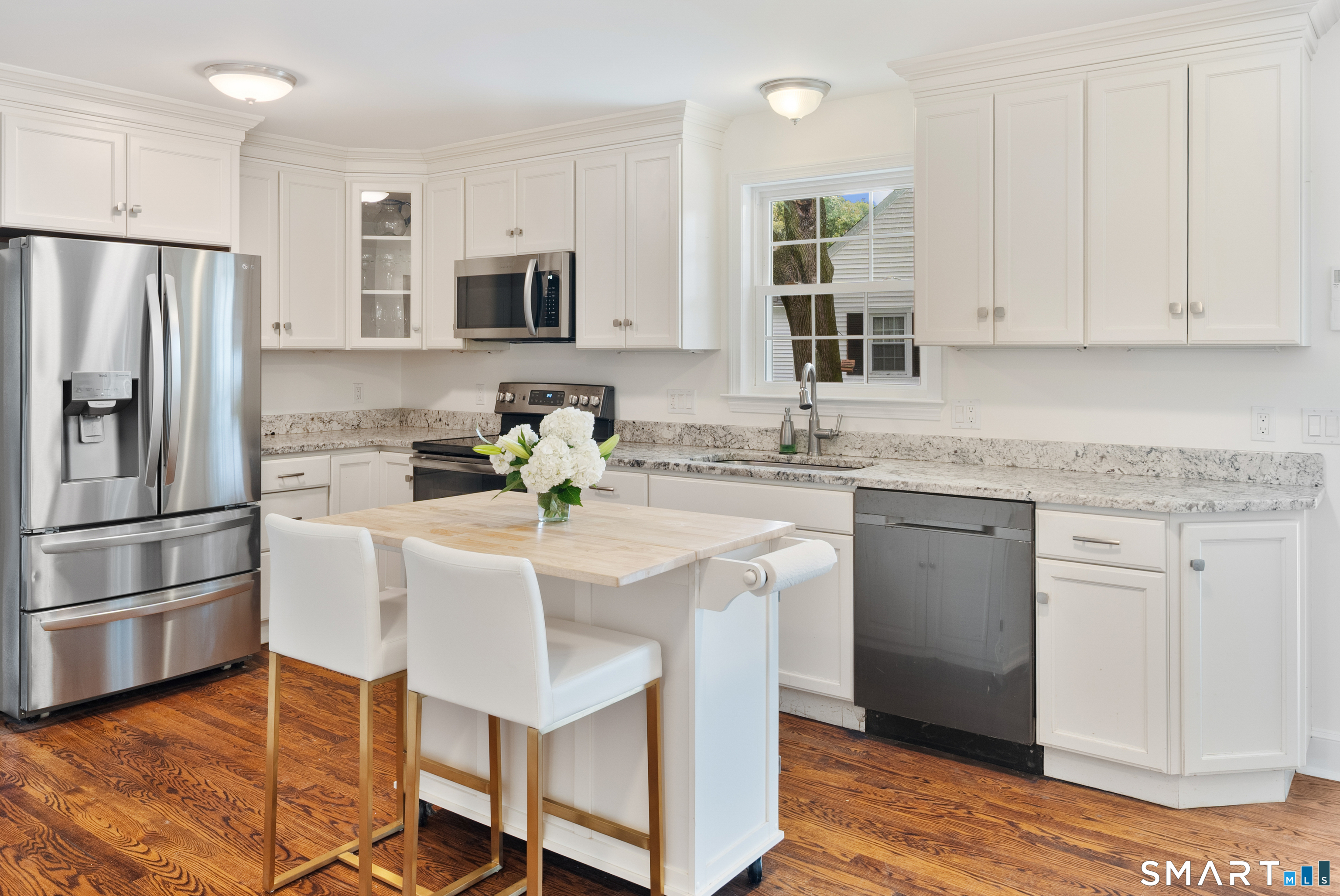 Bright white kitchen with stainless steel appliances, granite counters, a flower-topped island, and hardwood floors.