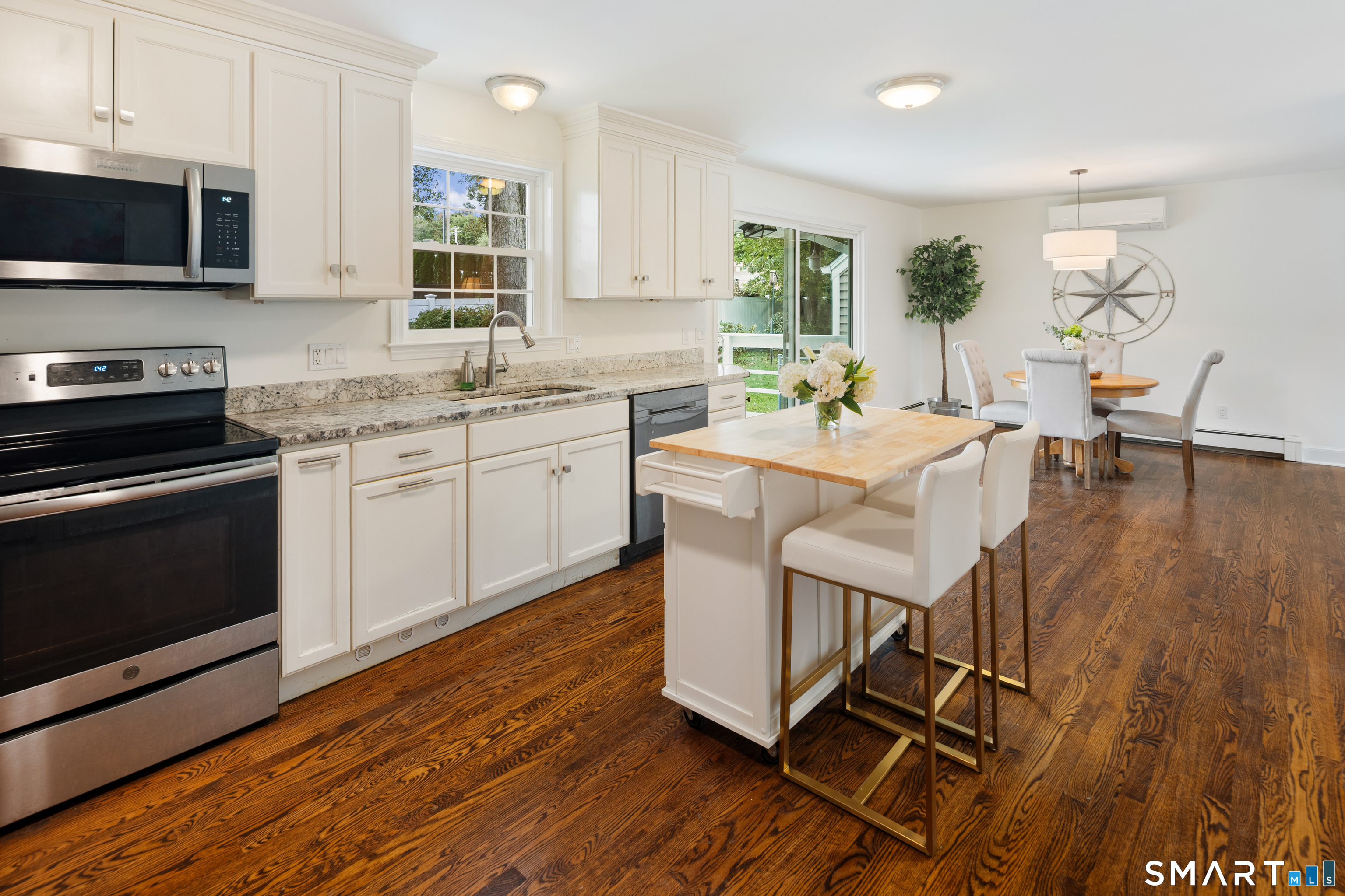Kitchen and dining area with a white island, granite counters, stainless appliances, and dark hardwood floors.