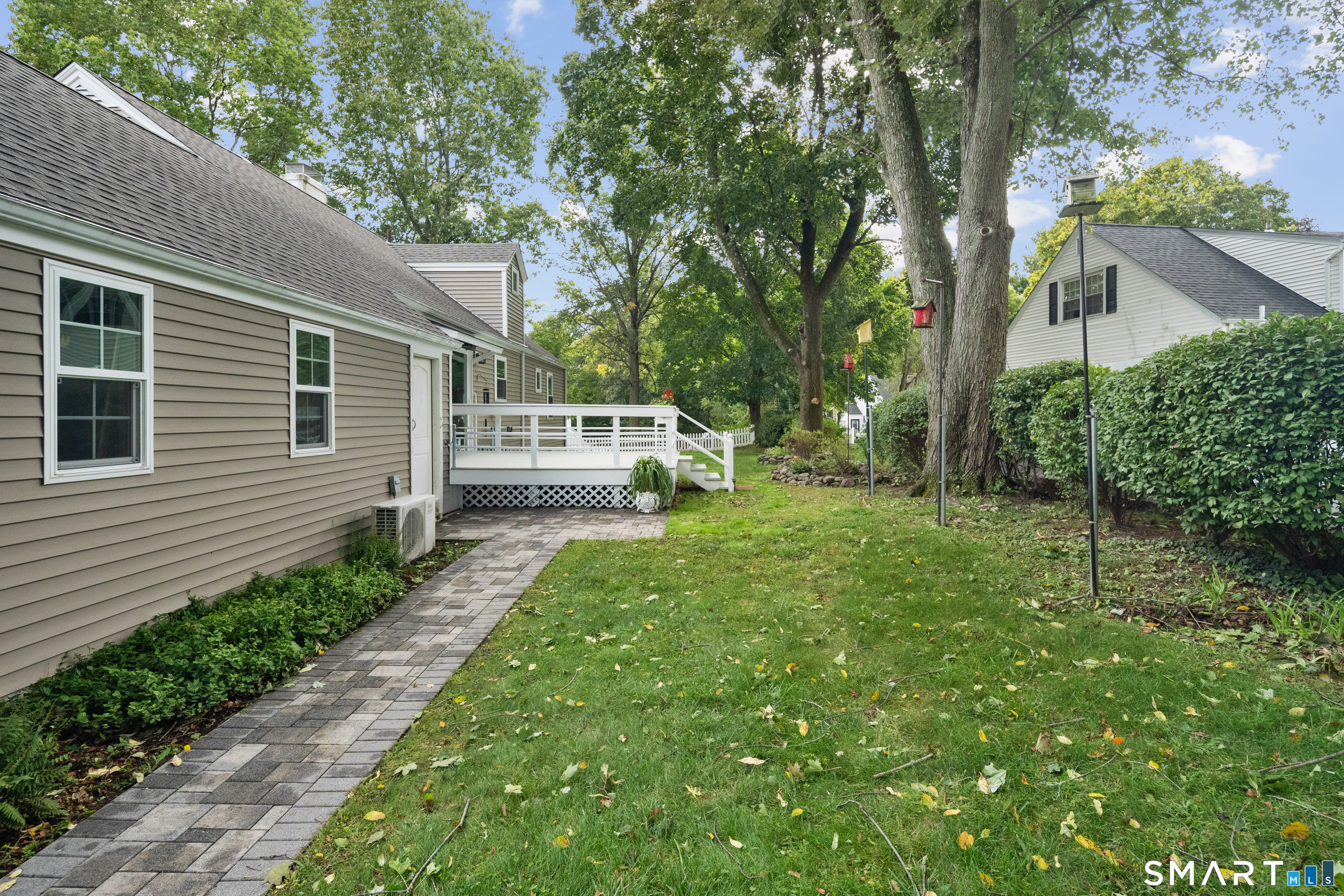 Backyard with a white-railed deck, paved walkway, lawn, and mature trees.