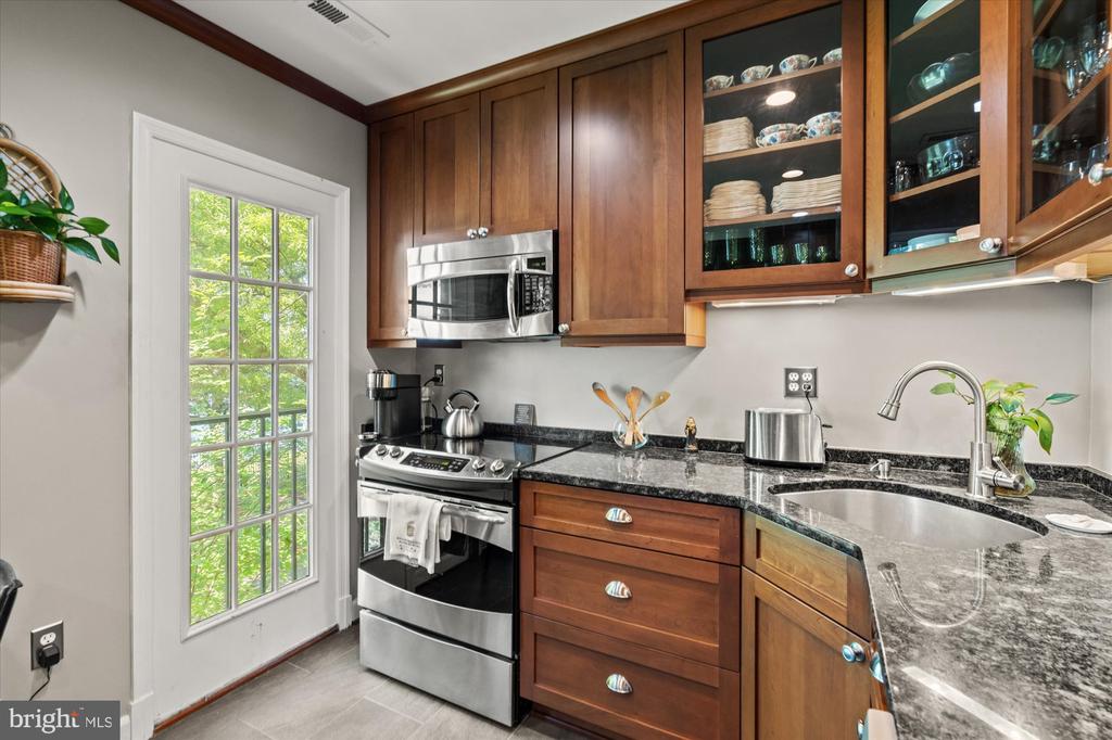 Kitchen with warm wood cabinets, dark stone counters, stainless steel appliances, and a tall glazed door.
