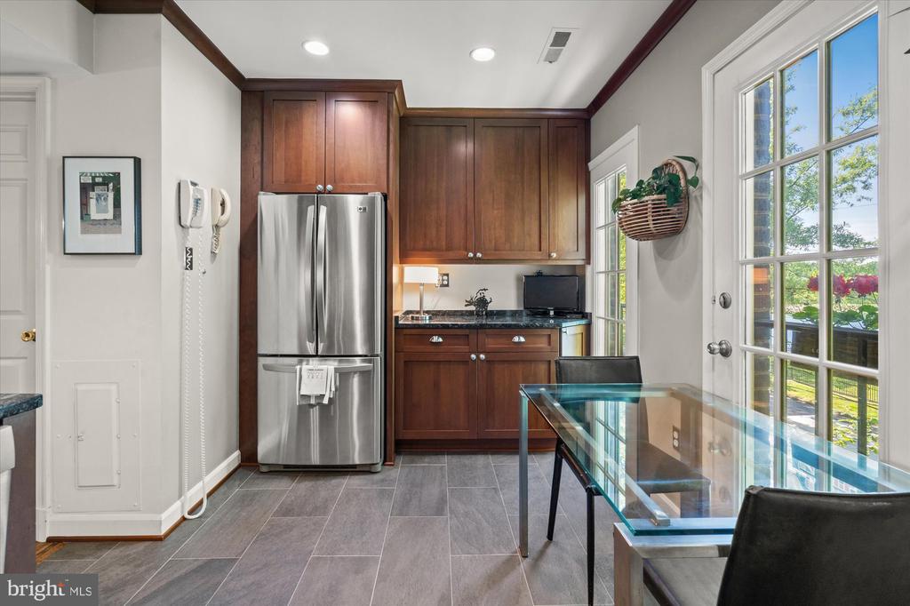 Kitchen with dark wood cabinets, stainless steel refrigerator, and glass dining table beside garden-facing French doors.
