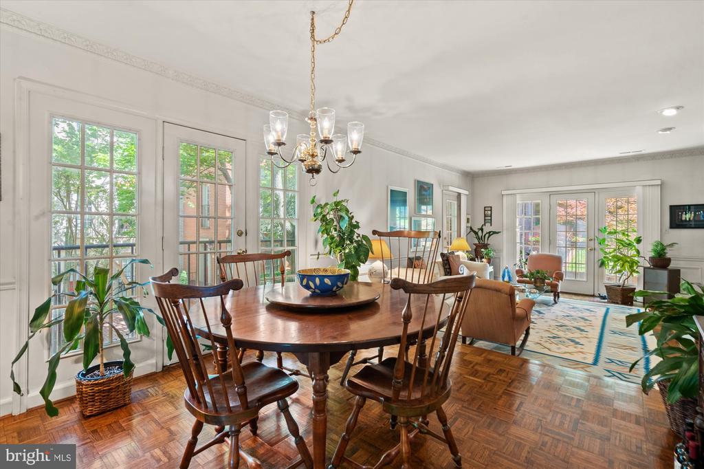 Dining room with a round wooden table, parquet floors, chandelier, and French doors.