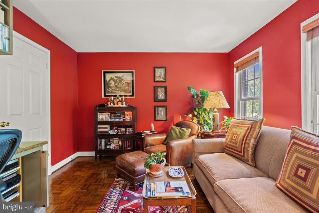 Living room with red walls, parquet floors, a beige sofa, and a leather armchair.