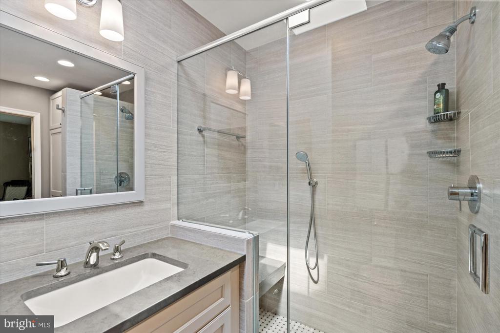 Bathroom with a glass-enclosed tiled shower beside a gray countertop and white sink vanity.