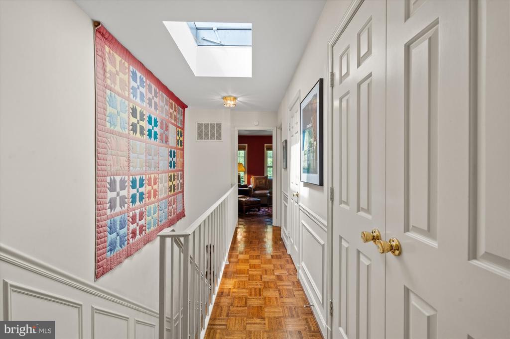 Upstairs hallway with a colorful patchwork quilt, parquet floor, and skylight.