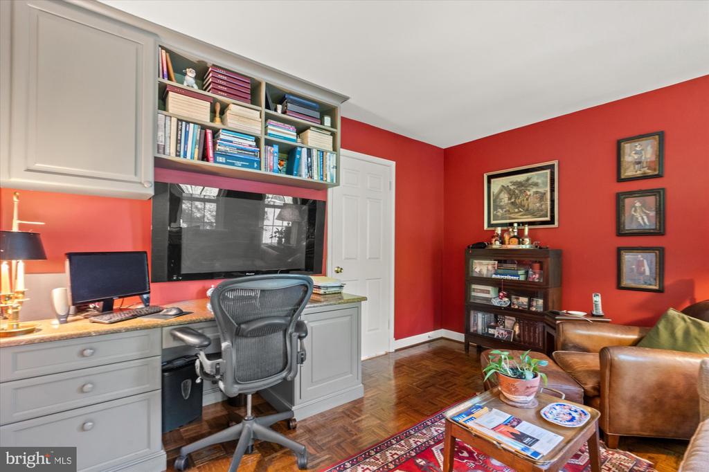 Furnished home office with built-in desk and bookshelves against bold red walls.