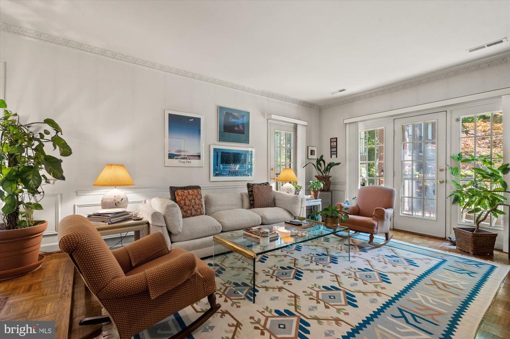 Living room with a cream sofa, brown armchairs, glass coffee table, and geometric rug.