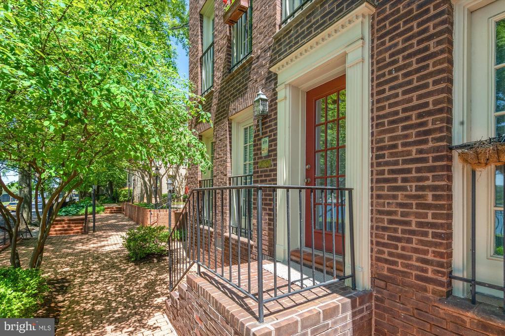 Brick residence entrance with a red glass-paneled door and raised stoop beside a leafy courtyard.