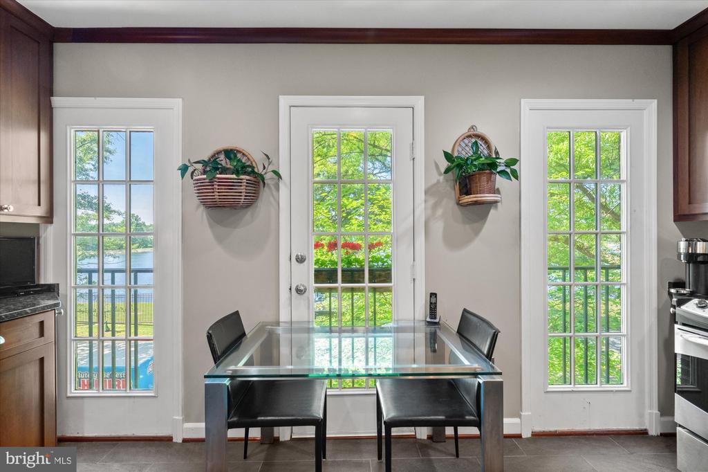 Dining area with a glass-top table, three tall windows, and water visible outside.