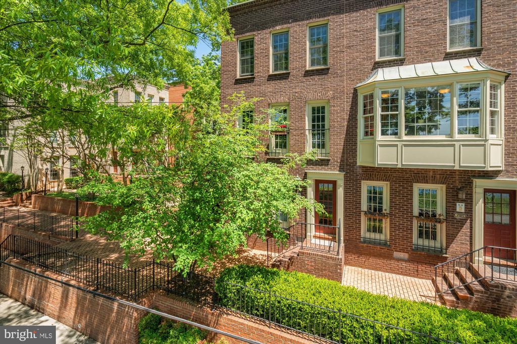 Brick townhouse exterior with a projecting bay window, fenced patio, and leafy landscaping.