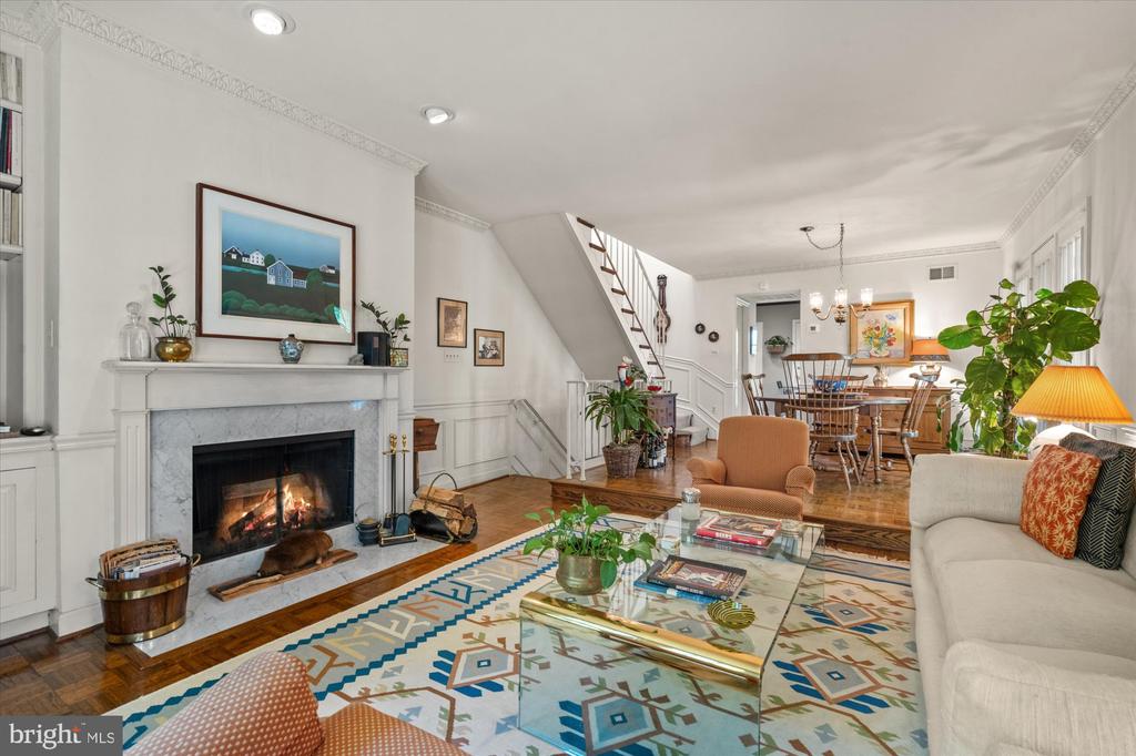 Living room with a marble fireplace, hardwood floors, and staircase beside the dining area.