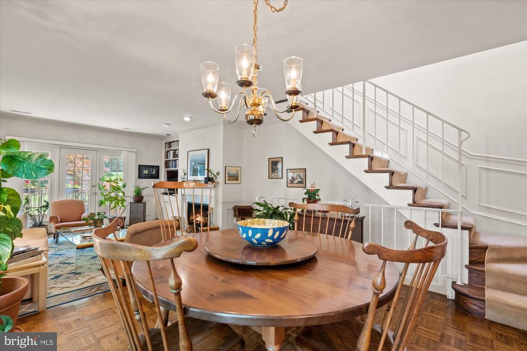 Dining room with a round wooden table, chandelier, and staircase beside an adjoining fireplace.