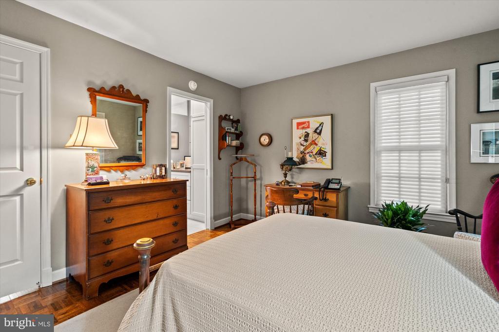 Furnished bedroom with a large bed, antique wooden dressers, a mirror, and parquet flooring.