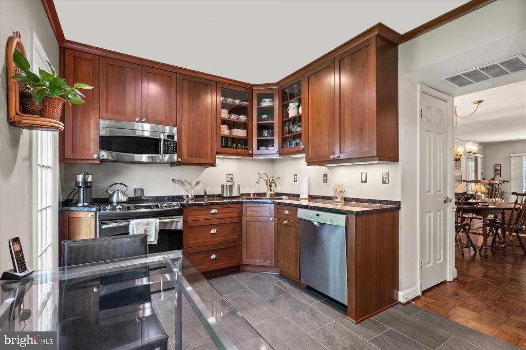 Kitchen with reddish-brown wood cabinets, granite counters, stainless steel appliances, and a glass dining table.