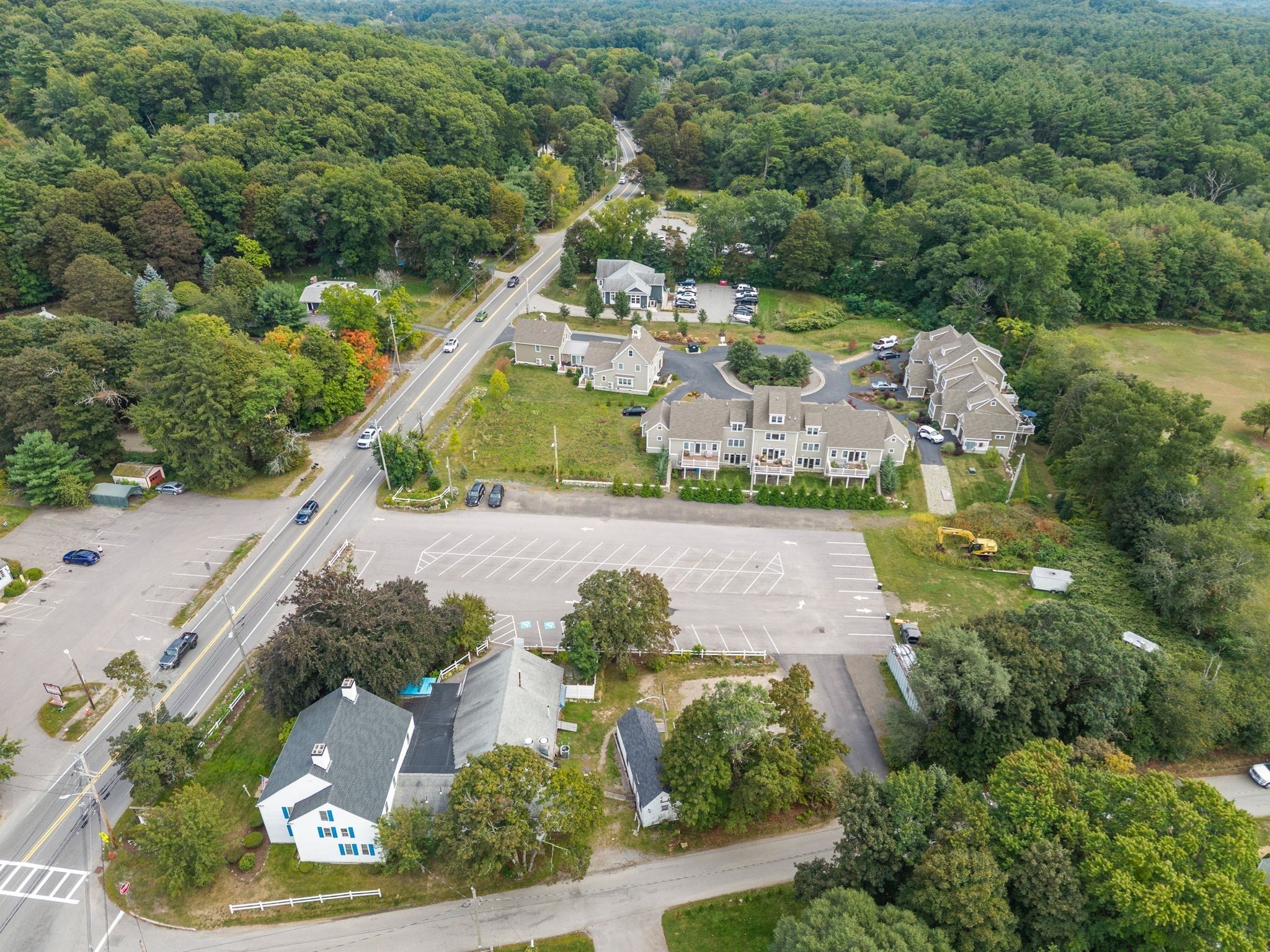 Aerial view of buildings beside a large parking lot and wooded surroundings.