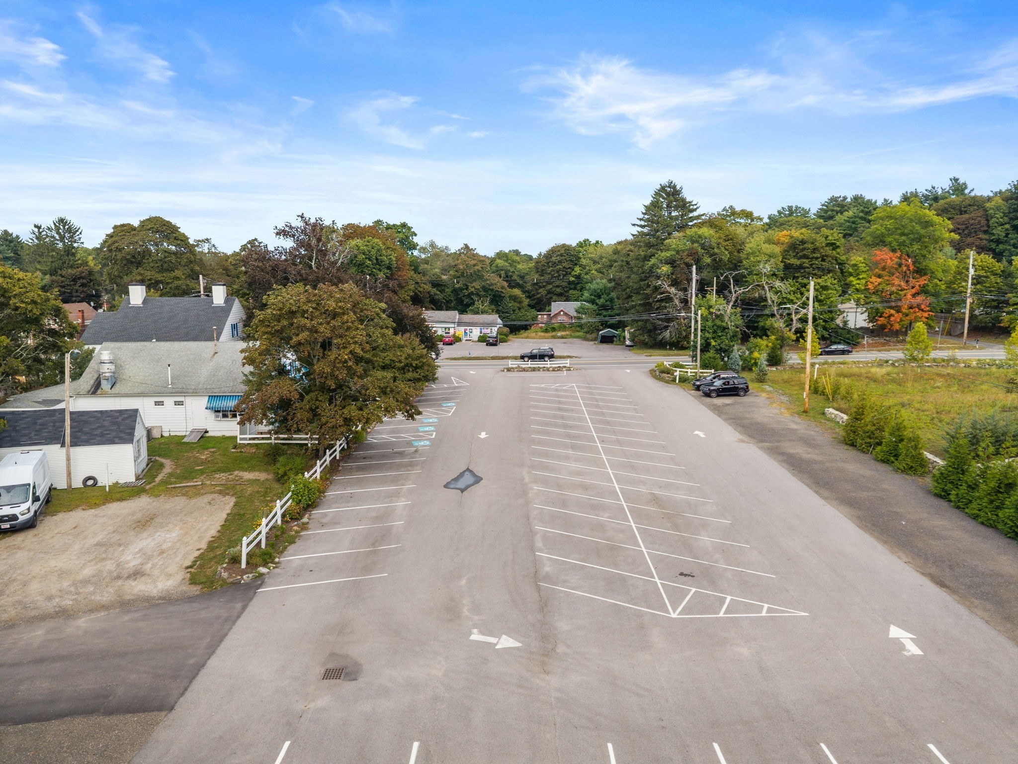 Aerial view of a marked parking lot beside a white building and autumn trees.