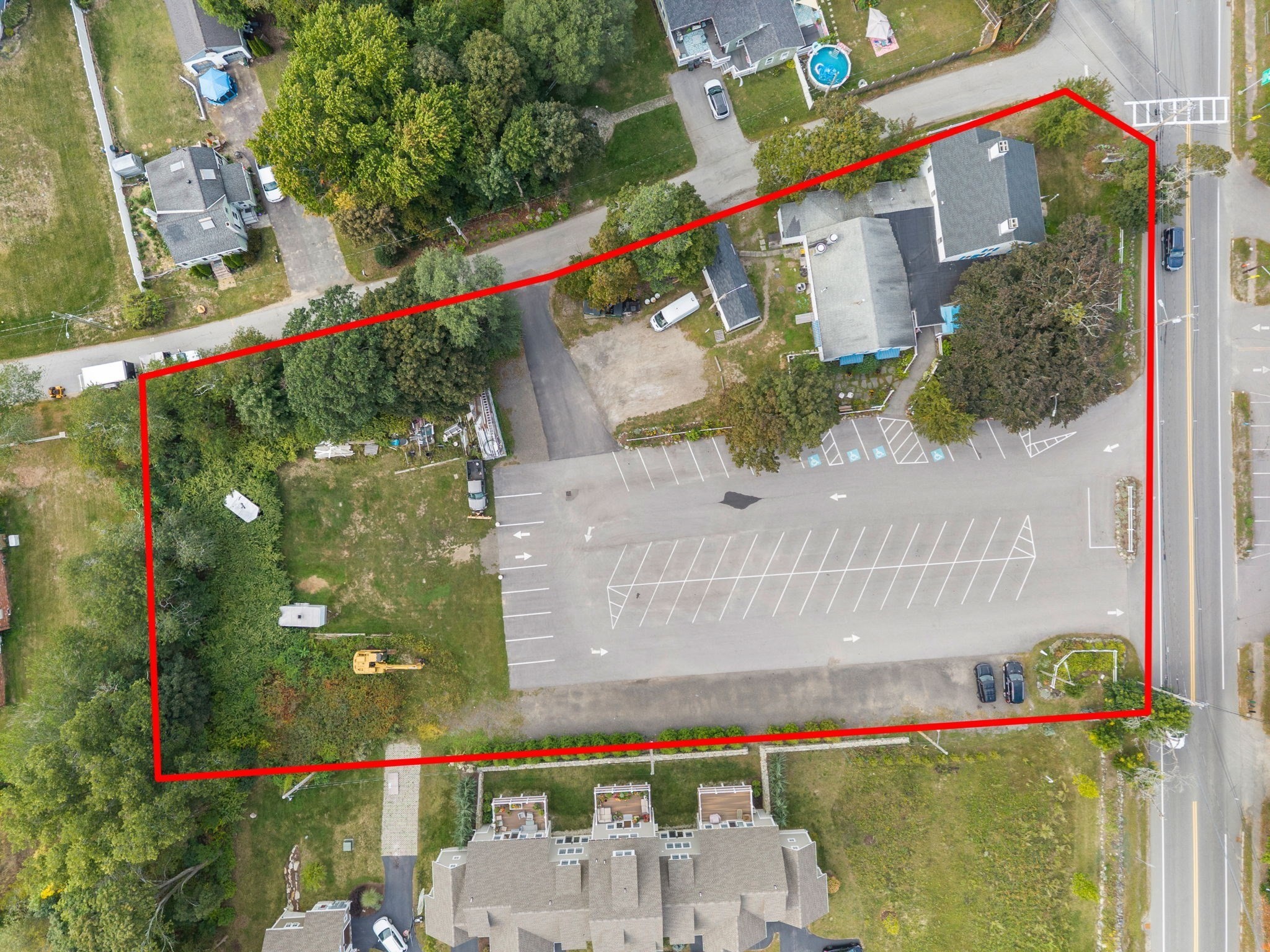 Aerial property with a large parking lot and buildings outlined in red beside a main road.