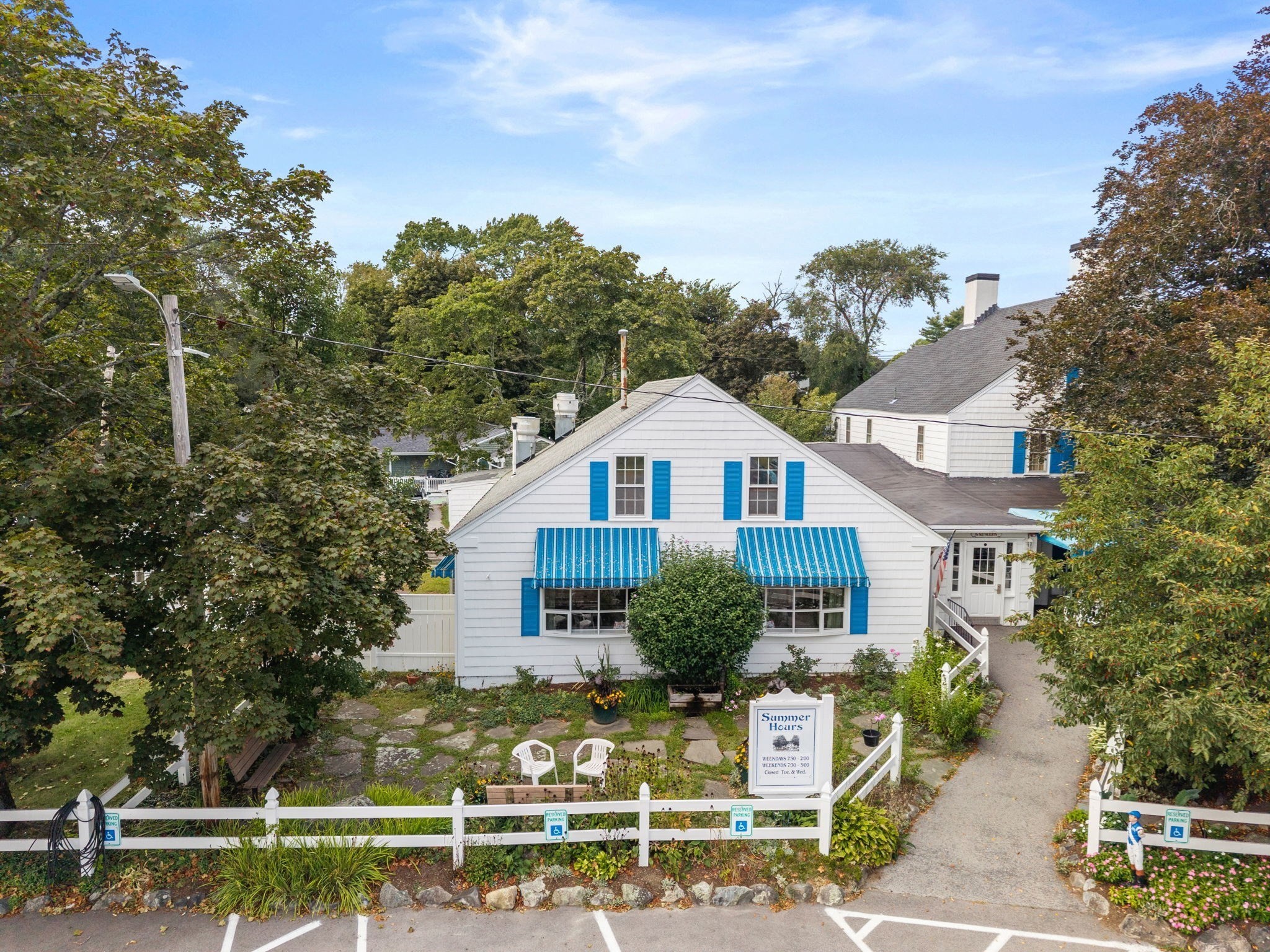 White building with blue shutters and striped awnings, front garden, and white picket fence.
