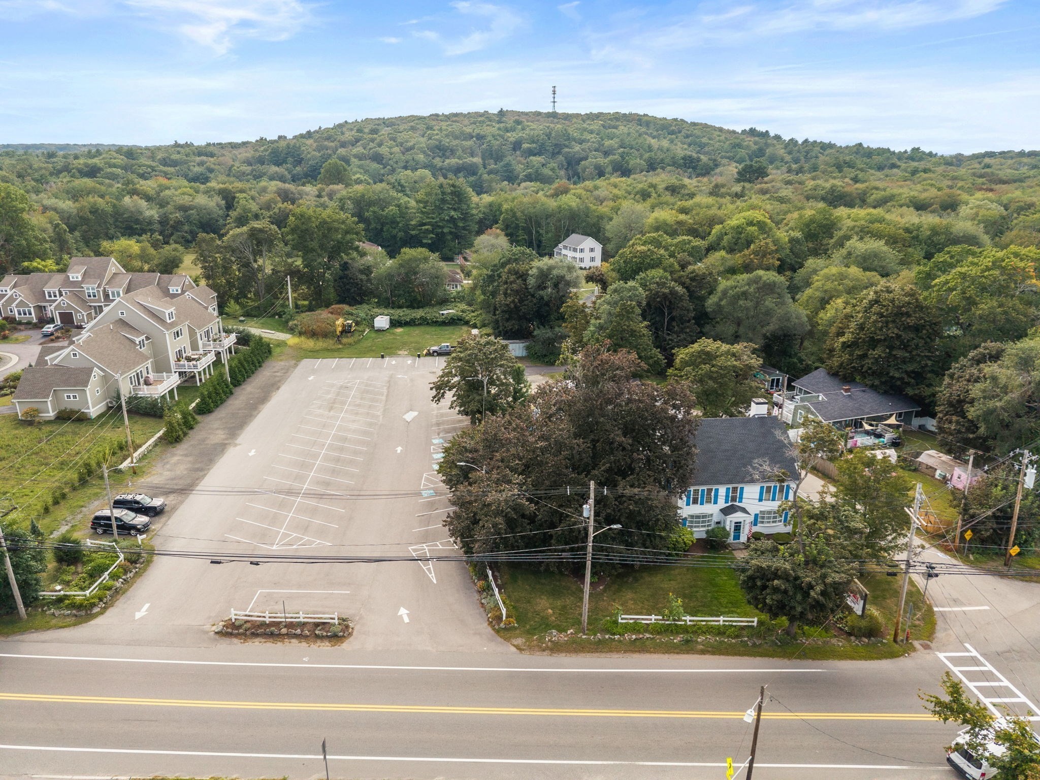 Aerial view of a parking lot and nearby homes, including a white house with blue trim.
