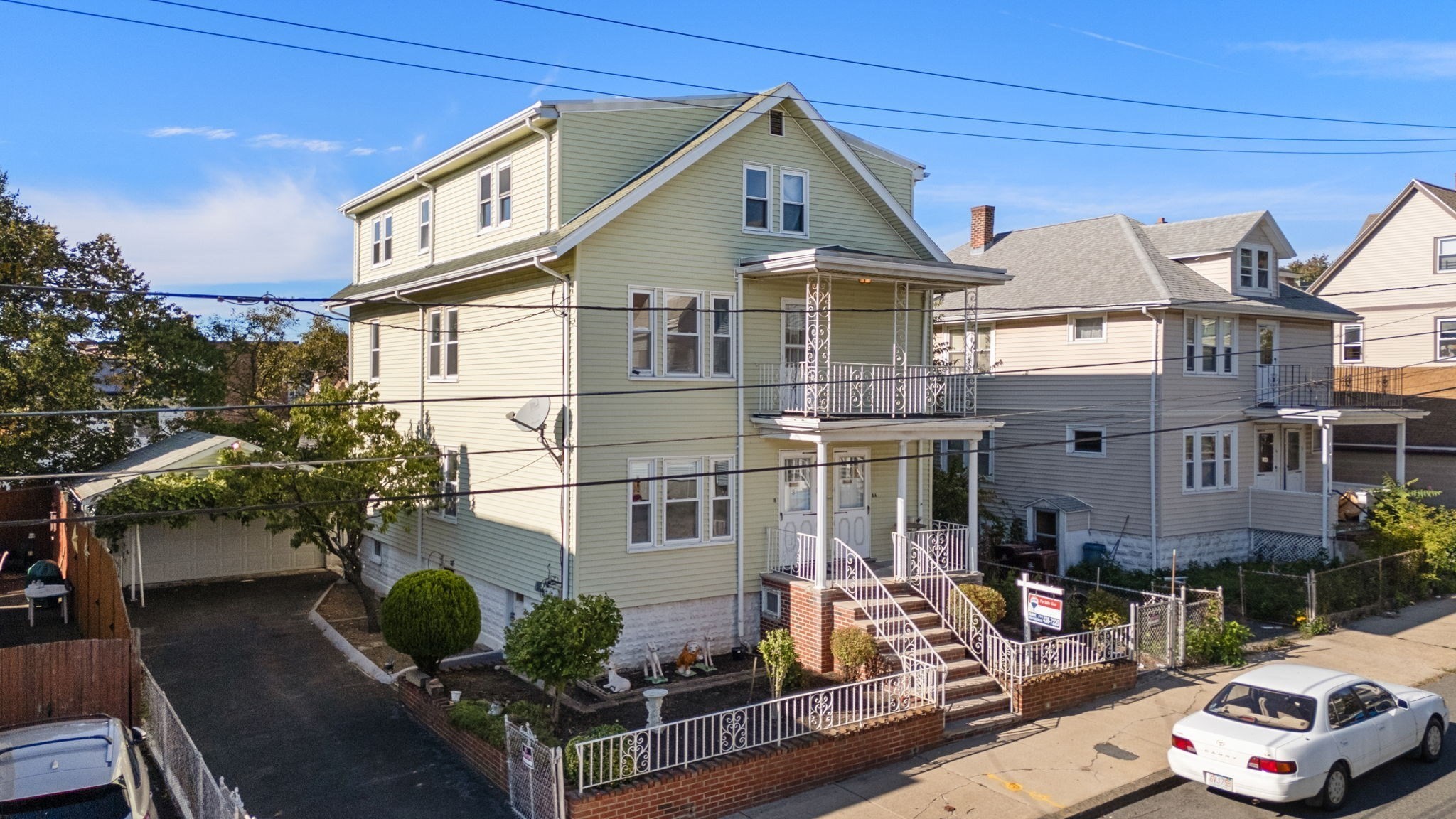 Pale green multi-story house with an ornate white porch, balcony, and brick steps.