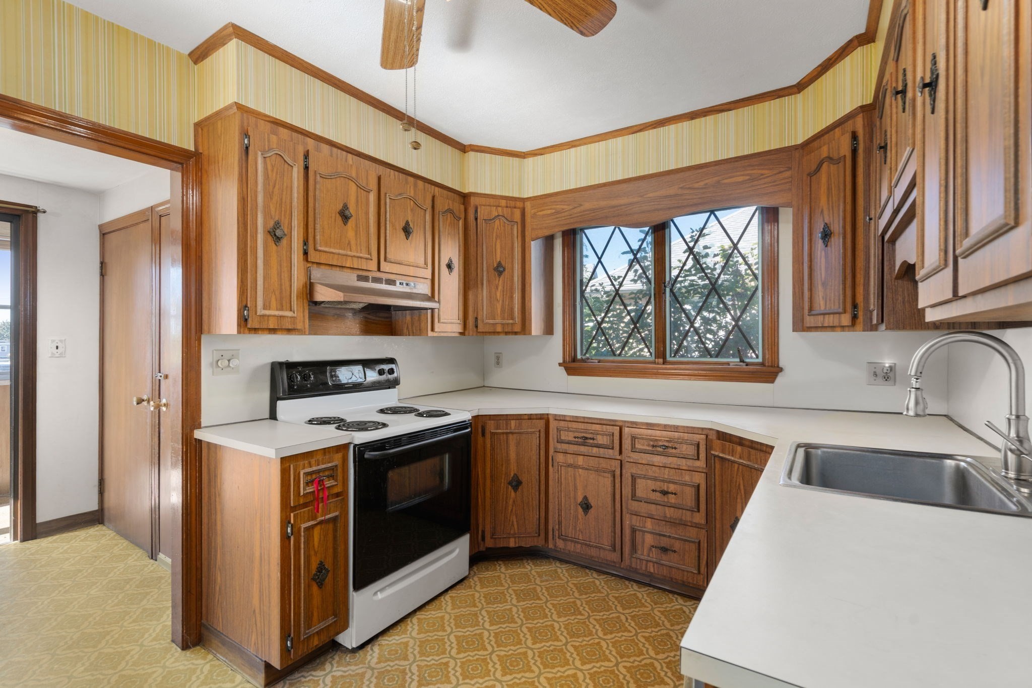 Kitchen with dark wood cabinets, white counters, diamond-pane windows, and a patterned floor.