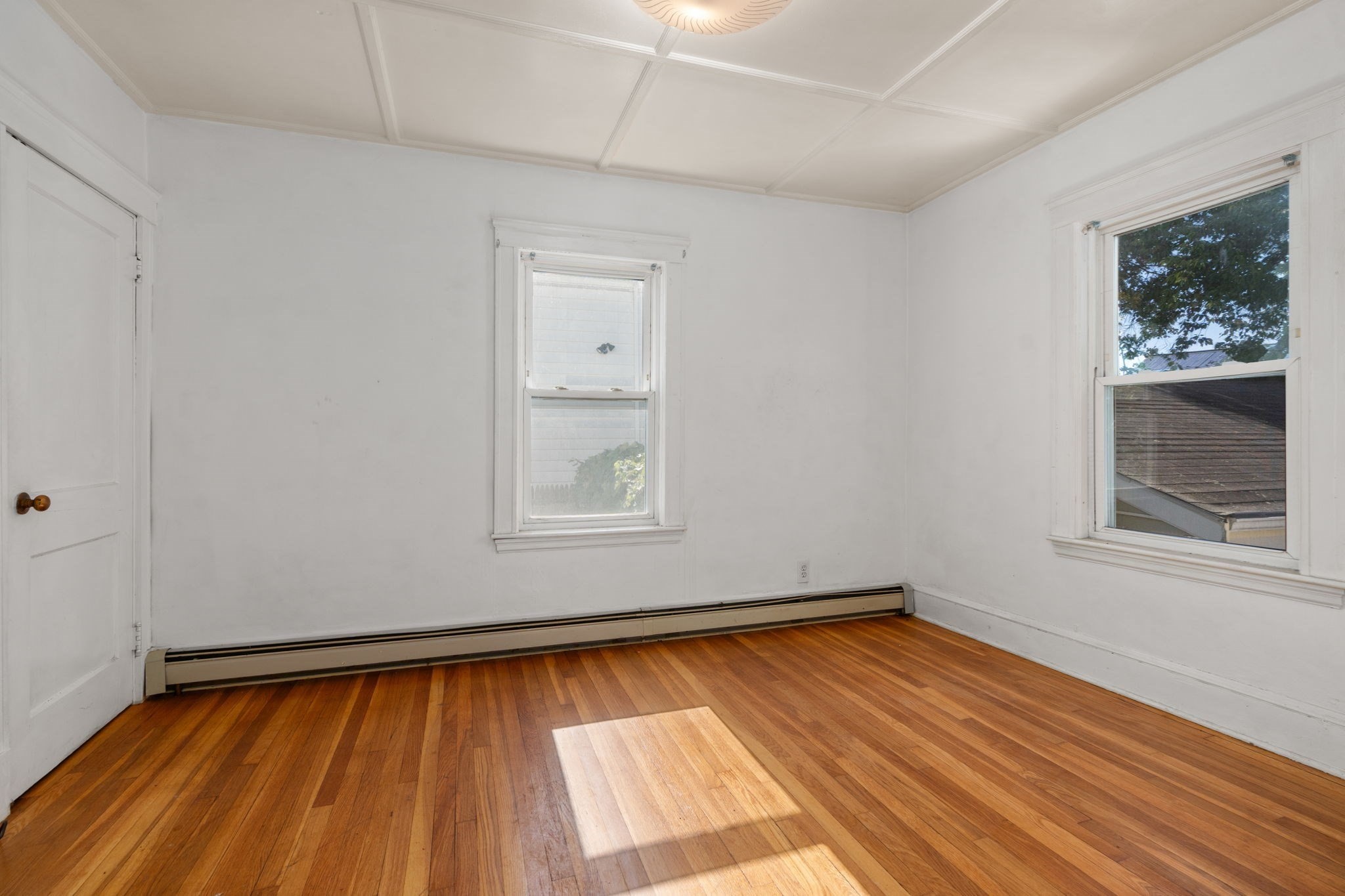 Vacant room with polished hardwood floors, two windows, and white paneled ceiling.