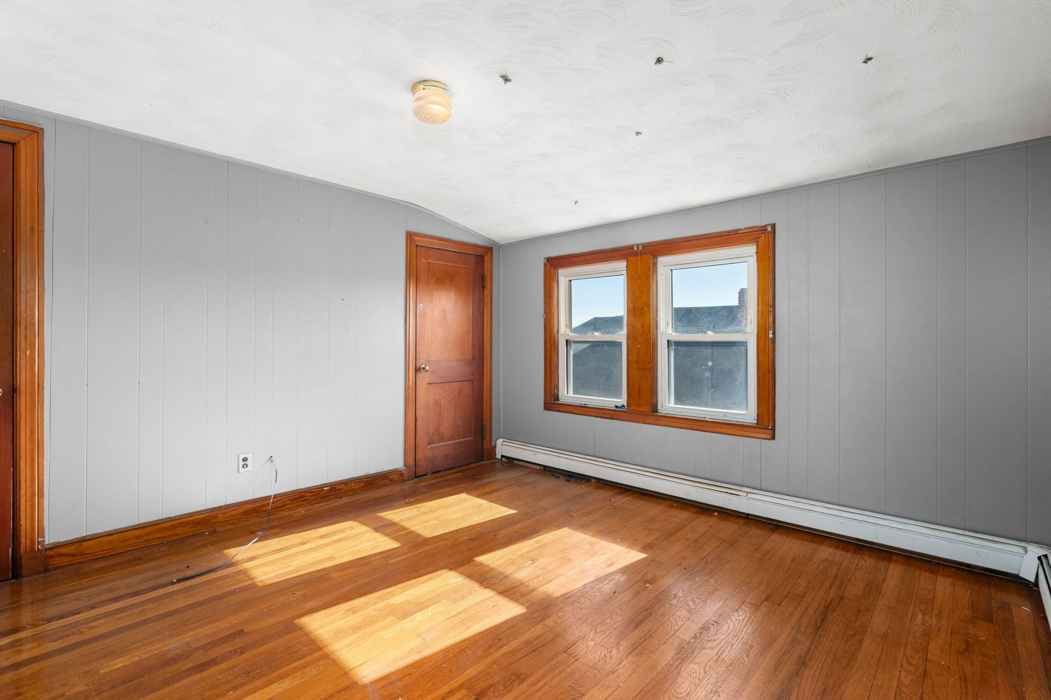 Empty room with hardwood floors, gray paneled walls, and two wood-trimmed windows.