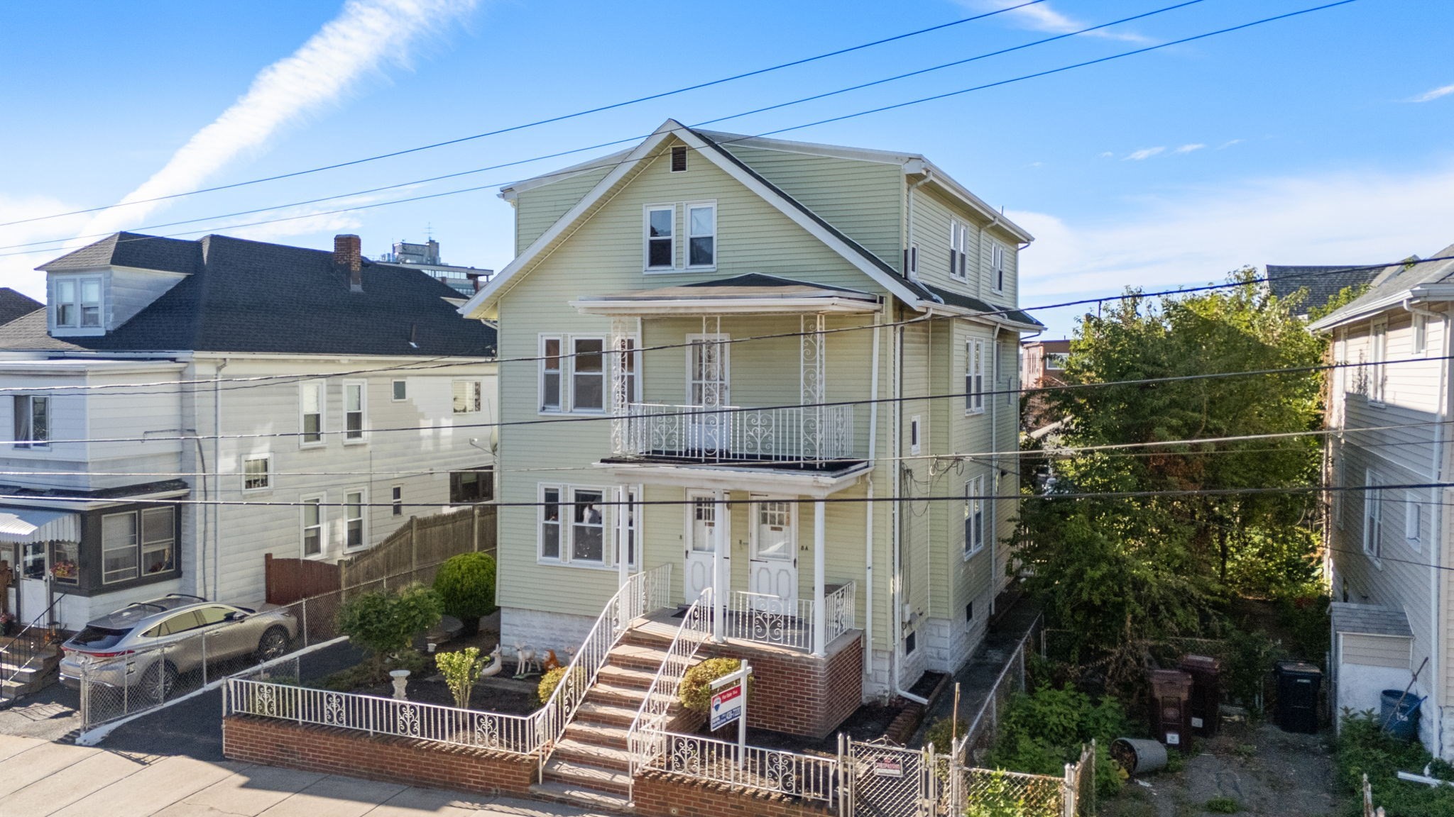 Pale green multi-story house with white trim, decorative porches, and brick front steps.