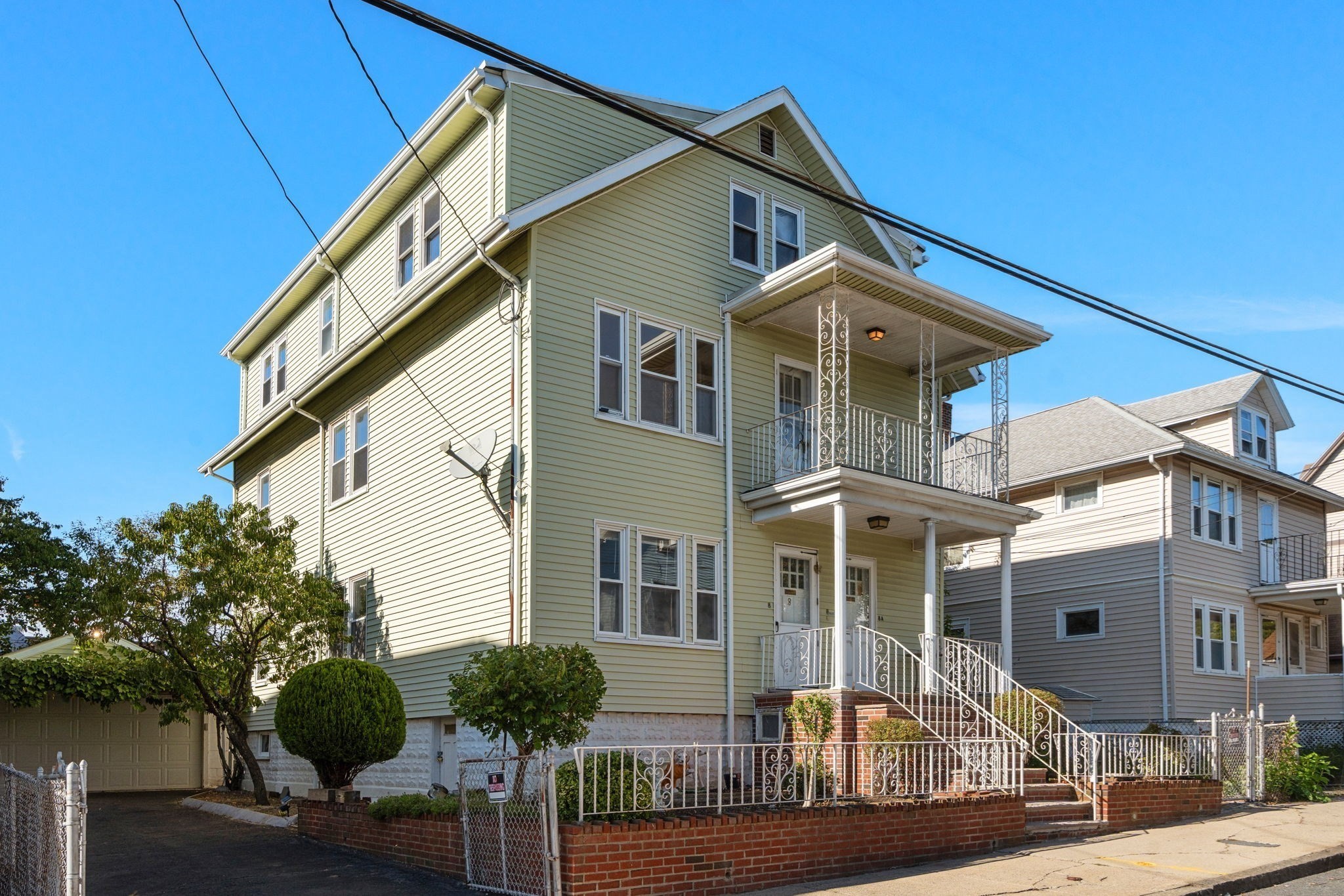 Three-story pale green house with ornate white porch railings and brick steps.