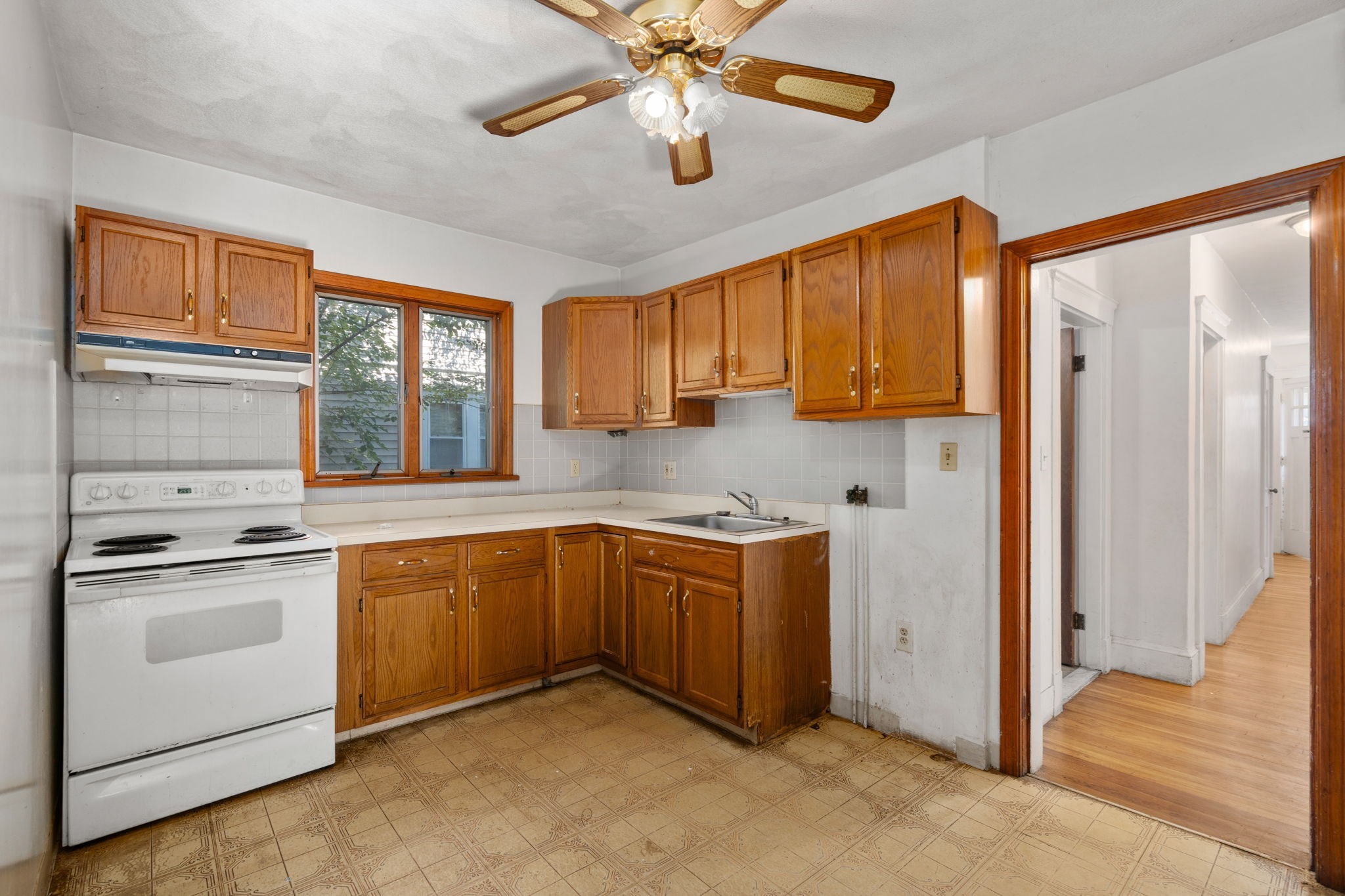 Kitchen with warm wood cabinets, a white electric range, and a window overlooking the yard.
