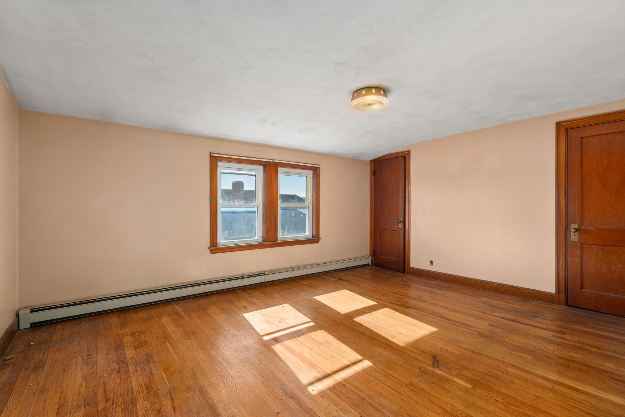 Empty room with hardwood floors, two windows, wooden doors, and sunlight across the floor.