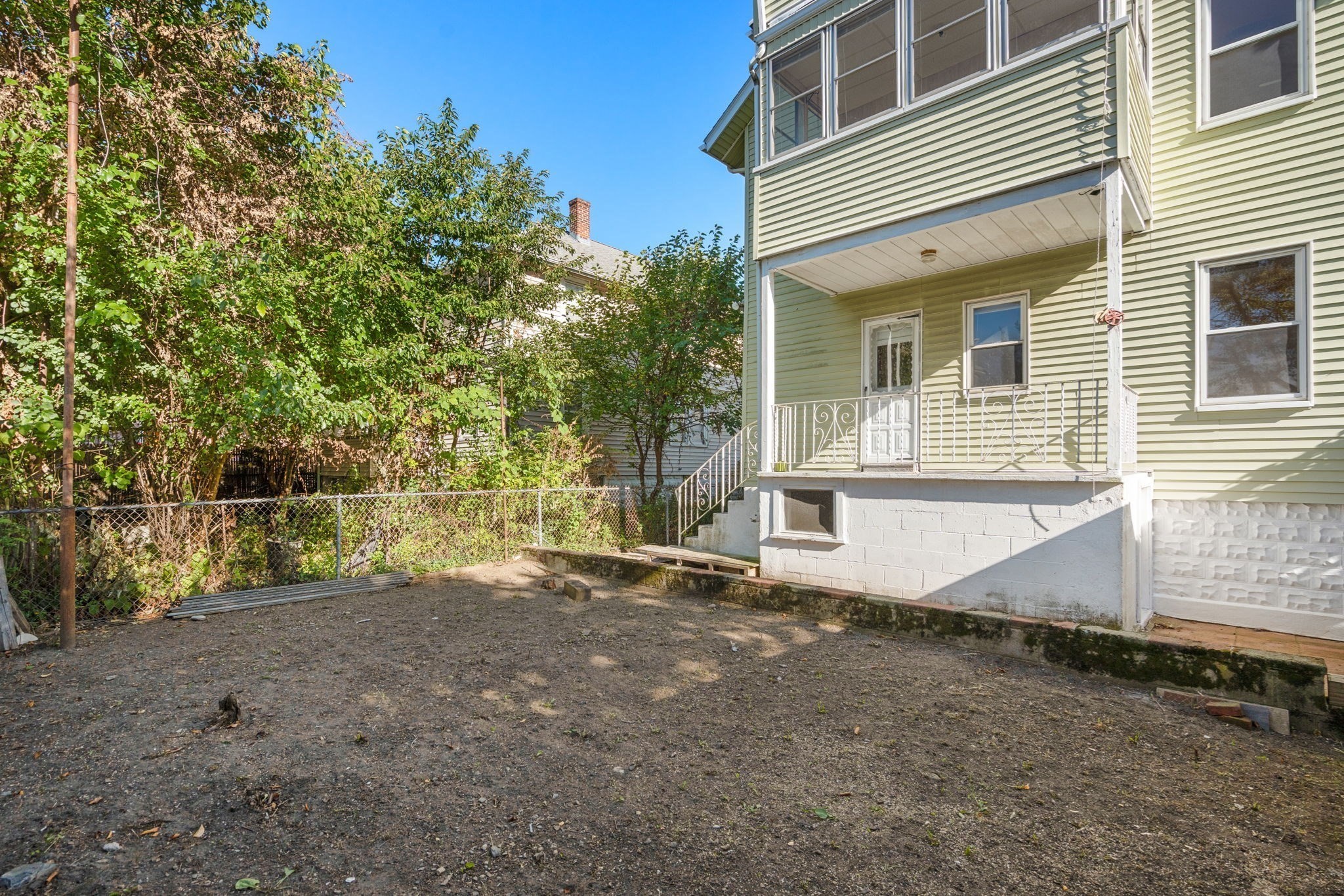 Rear of a light-green house with a covered porch and fenced, mostly bare backyard.