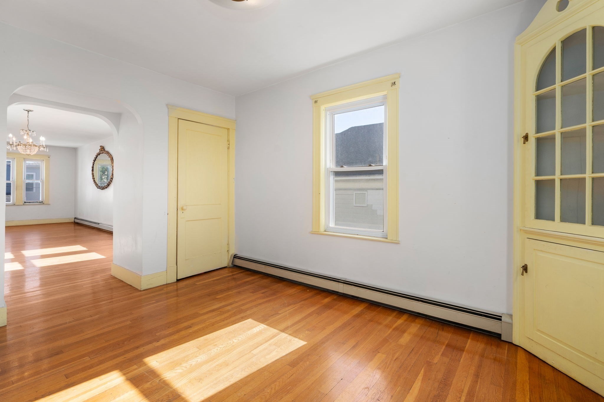 Empty room with hardwood floors, yellow trim, a glass-front cabinet, and an arched opening.