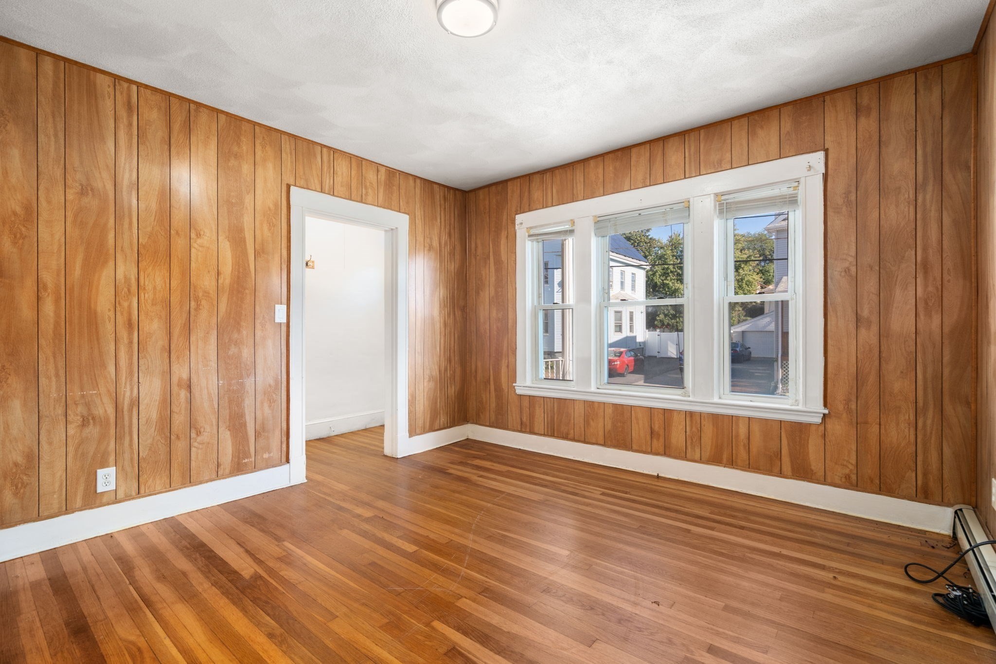 Empty room with wood-paneled walls, hardwood floors, and a large set of windows.