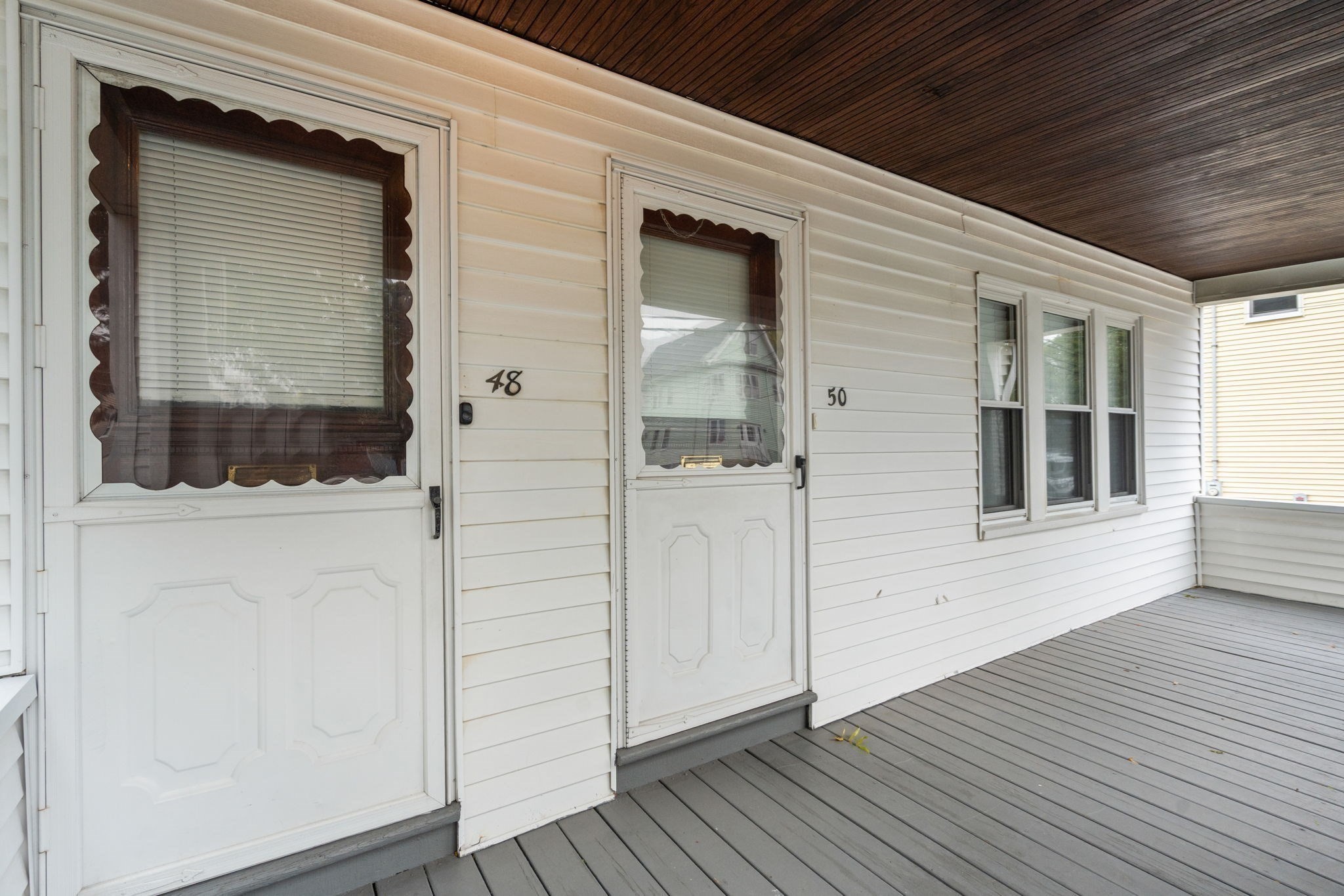 Covered porch with two white entry doors marked 48 and 50, gray decking, and dark wood ceiling.