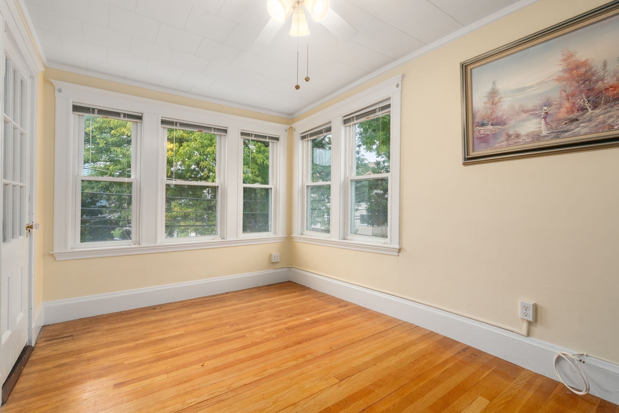 Empty room with hardwood floors and white-trimmed windows wrapping around two walls.