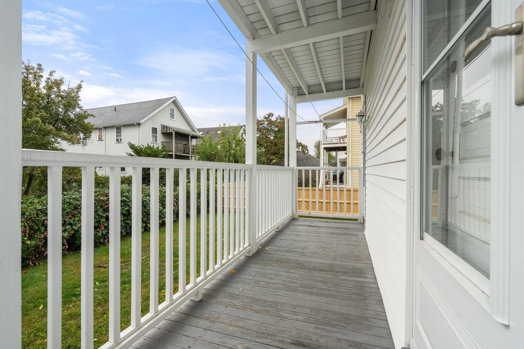 Covered wooden porch with white railings beside a white-sided home.