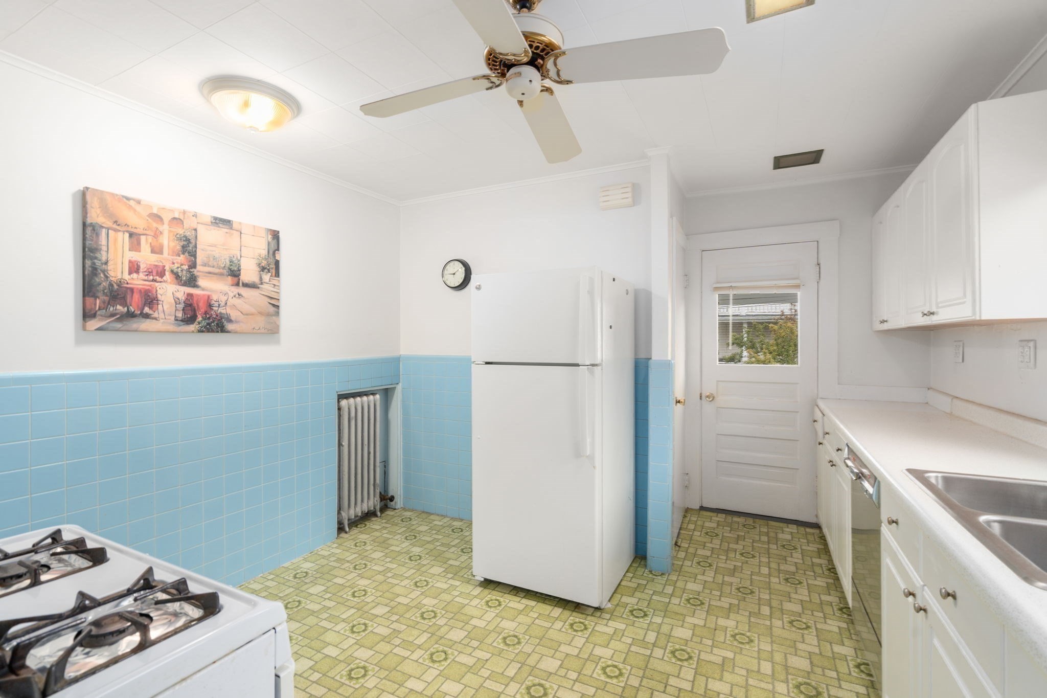 Kitchen with blue tile walls, patterned green floor, white refrigerator, and gas range.