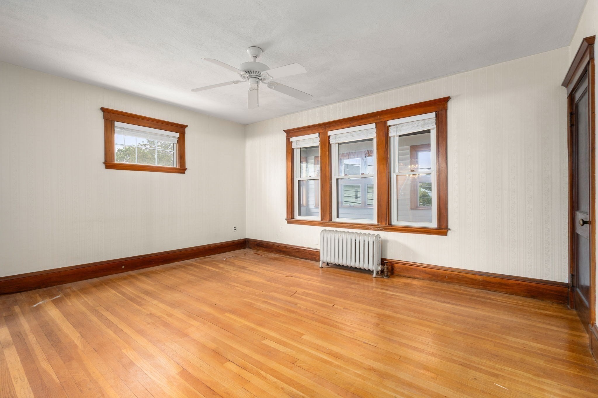 Empty room with polished hardwood floors, three tall windows, and a white radiator.
