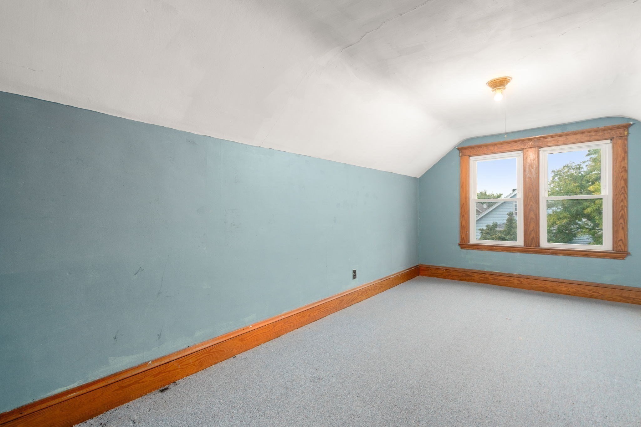 Empty blue room with gray carpet, a sloped ceiling, and two wood-trimmed windows.