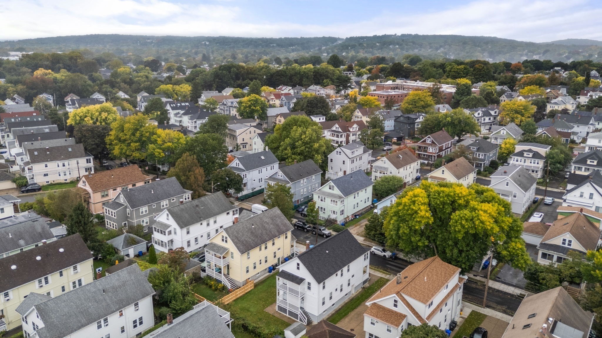 Aerial view of a tree-lined residential neighborhood with closely spaced homes and distant hills.