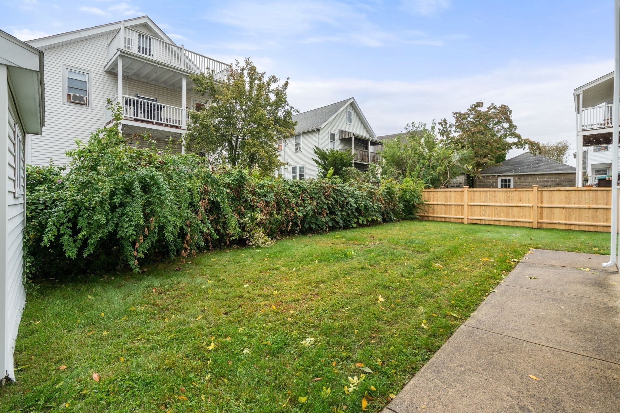 Backyard with a broad lawn, dense shrubs, wooden fence, and neighboring homes with balconies.