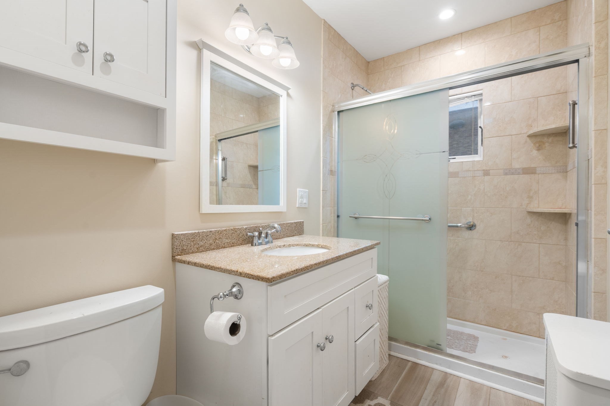 Bathroom with white vanity, beige tiled shower, and frosted sliding glass door.