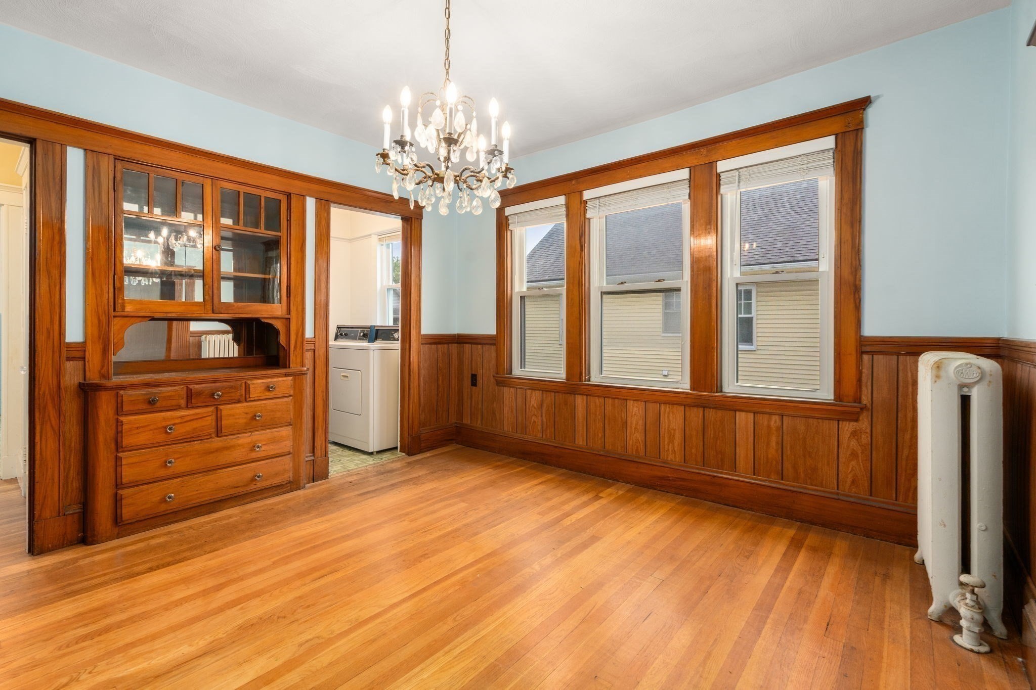Dining room with hardwood floors, wood-paneled walls, built-in china cabinet, and crystal chandelier.