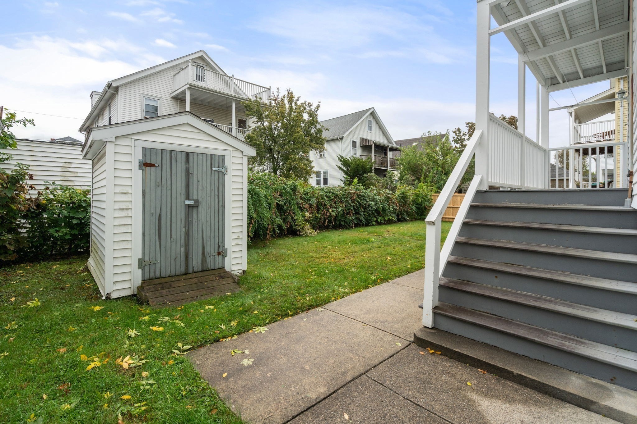 Backyard with a white shed, lawn, and raised deck with gray stairs.