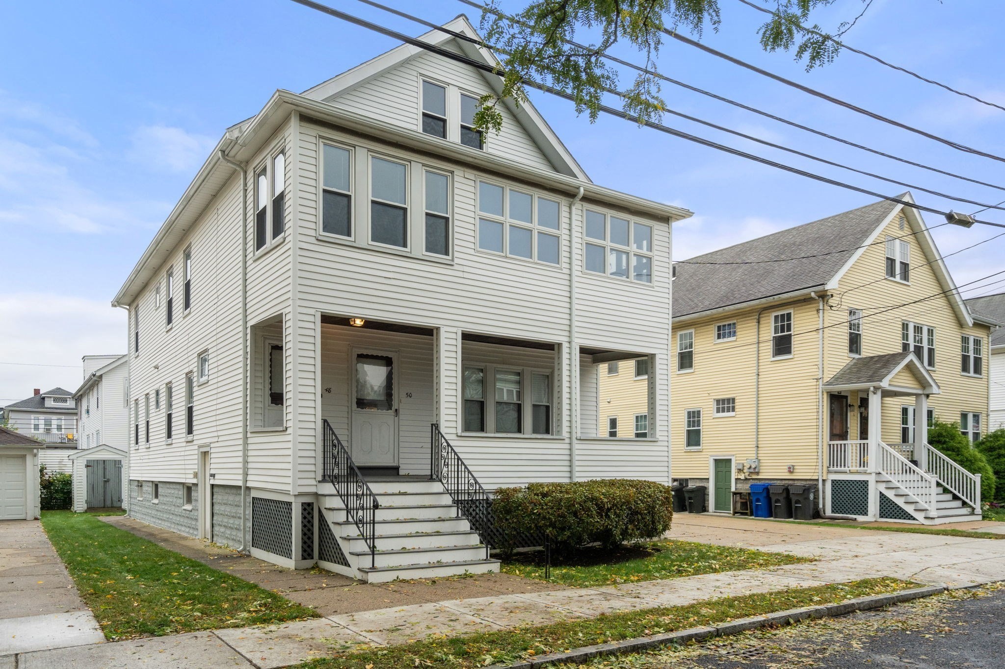 White two-story house with two numbered entrances, a covered porch, and black-railed front steps.