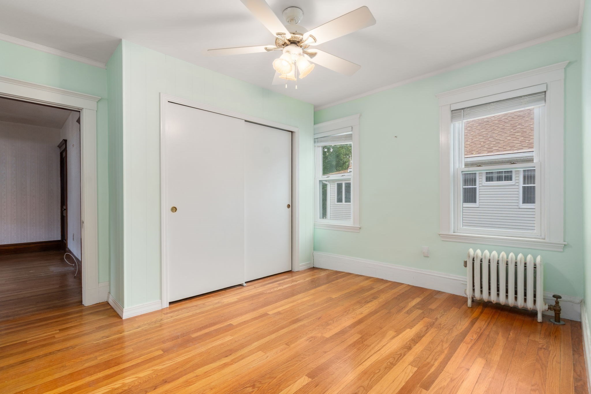Empty bedroom with mint-green walls, hardwood floors, a white closet, and a cast-iron radiator beneath two windows.