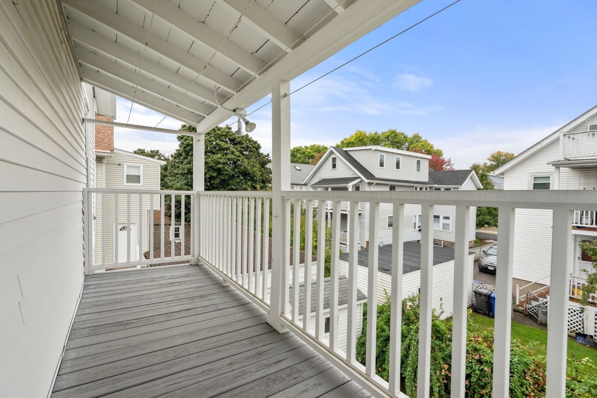 Covered balcony with gray decking and white railings overlooking nearby homes.