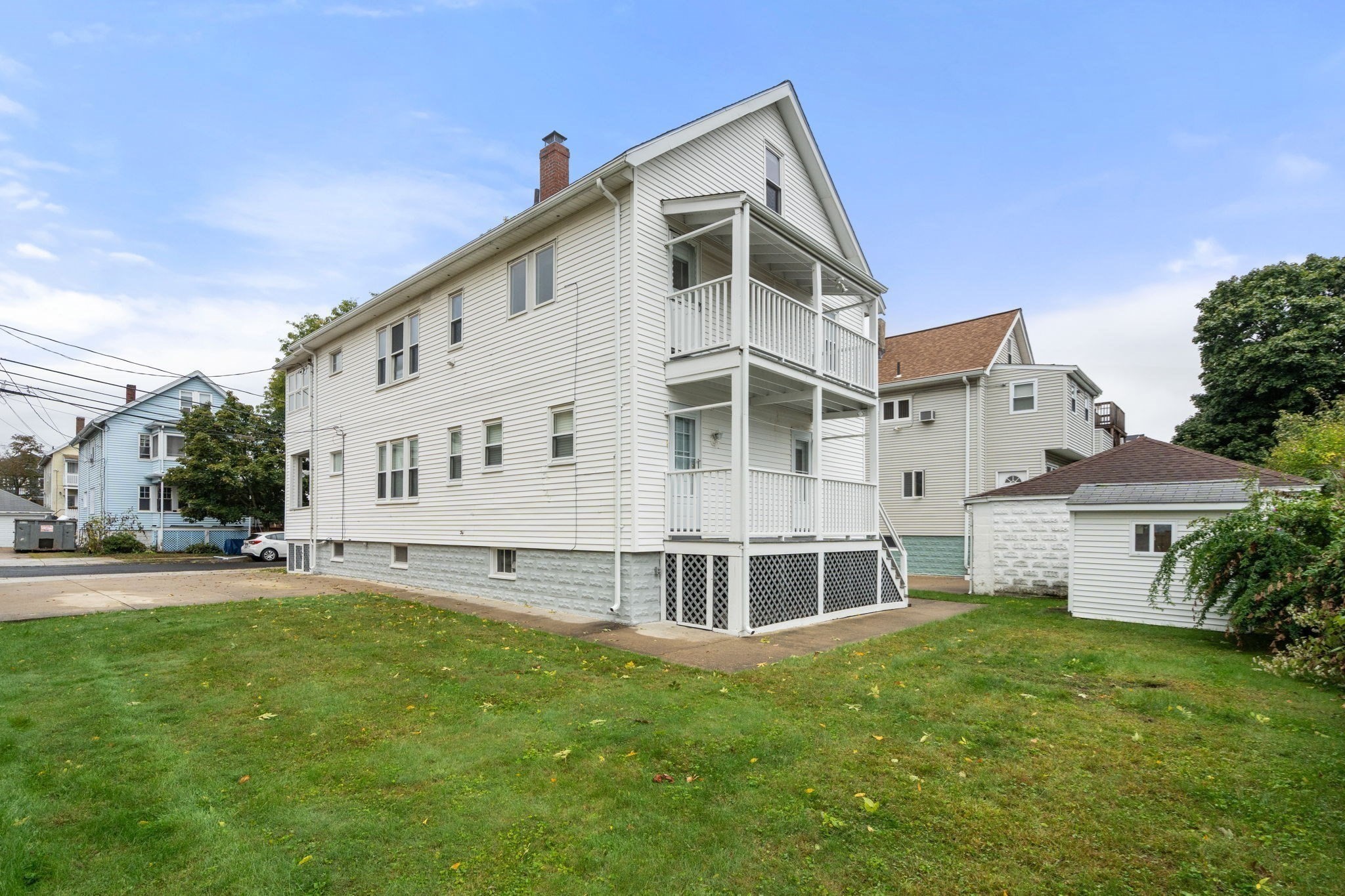 White multi-story house with stacked balconies and a broad grassy yard.