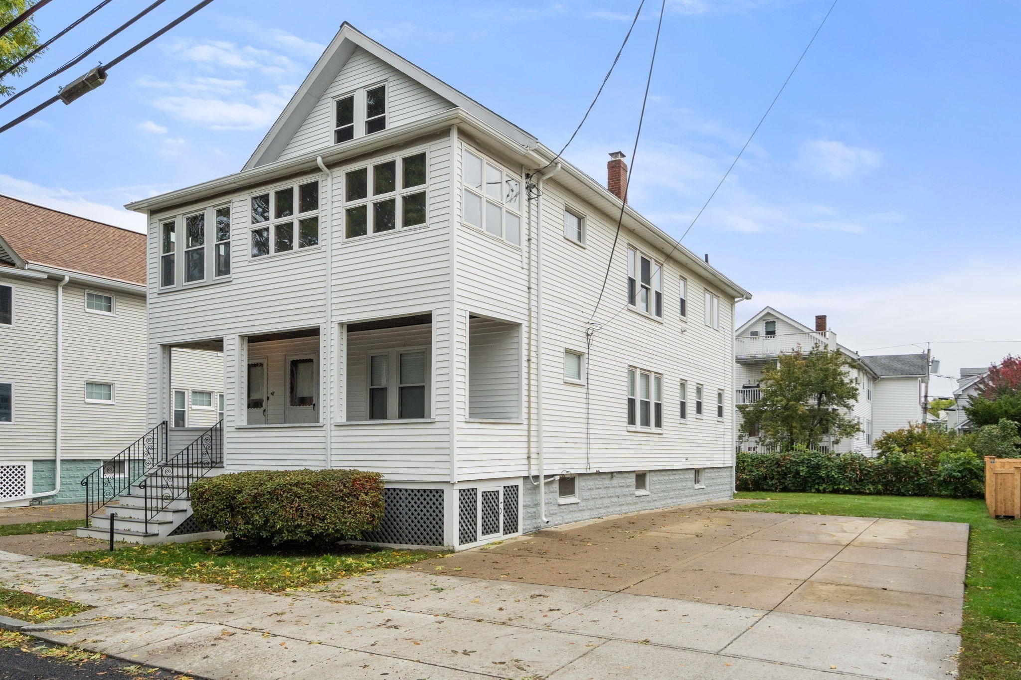 White multi-story house with a steep gable, covered raised porch, and paved driveway.